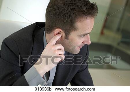 Stock Image - executive picking his ear during meeting. Fotosearch