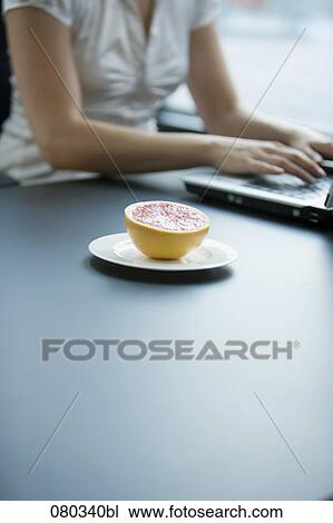 female employee working with laptop computer grapefruit on plate beside her View Large Photo Image Stock Image - female employee working with laptop computer grapefruit on plate beside her. Fotosearch