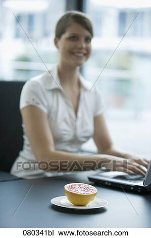 female employee working with laptop computer grapefruit on plate beside her View Large Photo Image Stock Image - female employee working with laptop computer grapefruit on plate beside her. Fotosearch