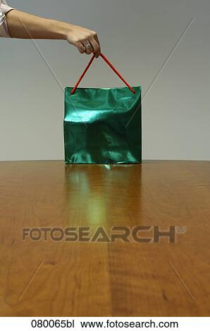 Stock Image - female hand taking shopping bag from table. Fotosearch