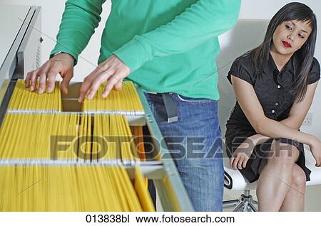 Stock Image - female office worker looking at buttocks of male colleague. Fotosearch