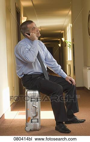 full body portrait of mature businessman sitting on suitcase in hotel corridor and talking on mobile phone View Large Photo Image Stock Image - full body portrait of mature businessman sitting on suitcase in hotel corridor and talking on mobile phone. Fotosearch