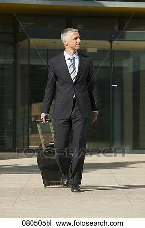 Stock Image - full body portrait of mature businessman with carry-on suitcase. Fotosearch