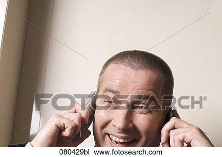 headshot of mature businessman listening to two mobile phones at once View Large Photo Image Stock Image - headshot of mature businessman listening to two mobile phones at once. Fotosearch