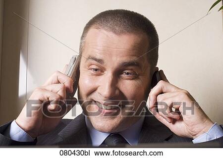 headshot of mature businessman listening to two mobile phones at once View Large Photo Image Stock Image - headshot of mature businessman listening to two mobile phones at once. Fotosearch