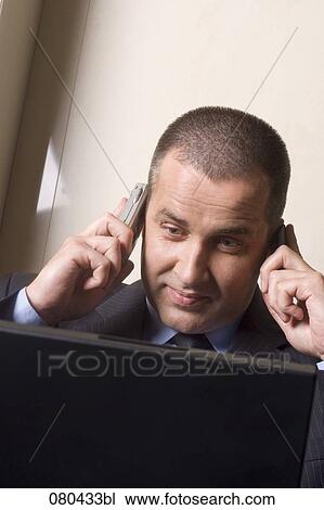 headshot of mature businessman listening to two mobile phones at once and looking at screen of laptop computer View Large Photo Image Stock Image - headshot of mature businessman listening to two mobile phones at once and looking at screen of laptop computer. Fotosearch