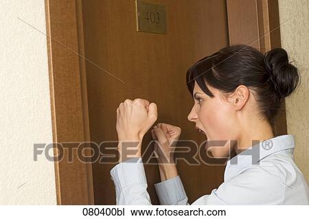 Stock Image - headshot of young businesswoman knocking angrily against door of hotel room. Fotosearch