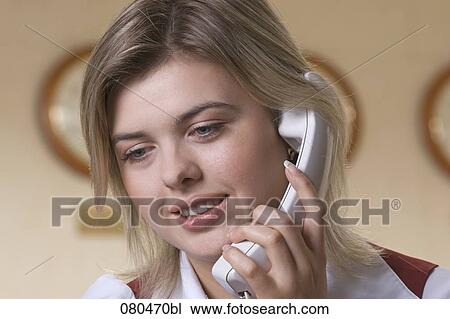 Stock Image - headshot of young hotel receptionist talking on telephone. Fotosearch