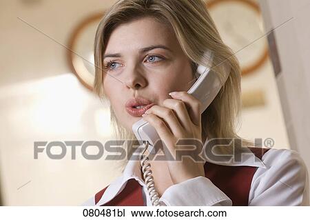 Stock Image - headshot of young hotel receptionist talking on telephone. Fotosearch
