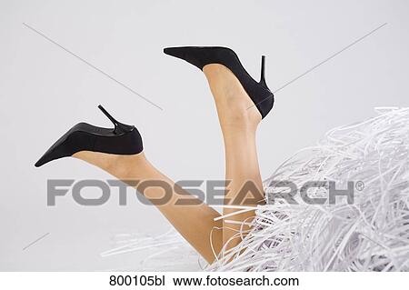 Stock Image - legs of young woman buried under shredded paper. Fotosearch