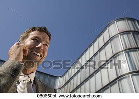 low angle portrait of businessman talking on mobile phone in front of office building View Large Photo Image Stock Image - low angle portrait of businessman talking on mobile phone in front of office building. Fotosearch