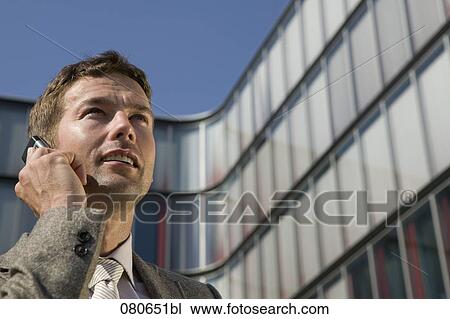 low angle portrait of businessman talking on mobile phone in front of office building View Large Photo Image Stock Image - low angle portrait of businessman talking on mobile phone in front of office building. Fotosearch