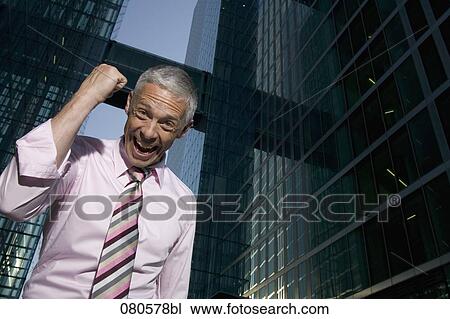 Stock Image - low angle portrait of mature businessman in front of office building celebrating. Fotosearch