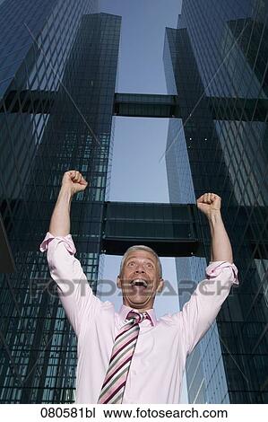 Stock Image - low angle portrait of mature businessman in front of office building celebrating. Fotosearch