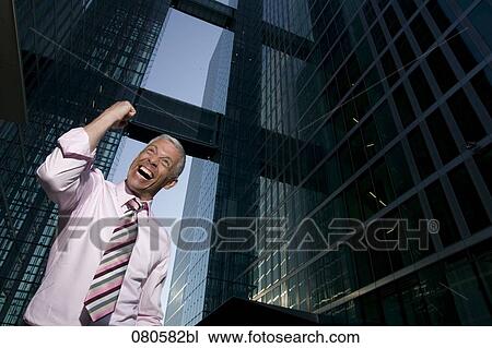 Stock Image - low angle portrait of mature businessman in front of office building celebrating. Fotosearch