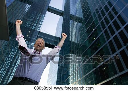 Stock Image - low angle portrait of mature businessman in front of office building celebrating. Fotosearch