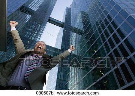 Stock Image - low angle portrait of mature businessman in front of office building celebrating. Fotosearch