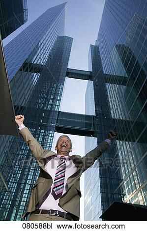 Stock Image - low angle portrait of mature businessman in front of office building celebrating. Fotosearch