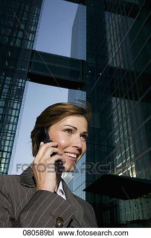 Stock Image - low angle portrait of mature businesswoman talking on mobile phone in front of office building. Fotosearch