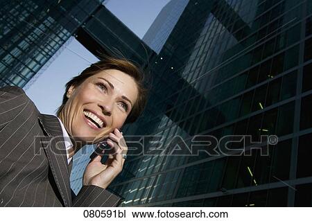 Stock Image - low angle portrait of mature businesswoman talking on mobile phone in front of office building. Fotosearch