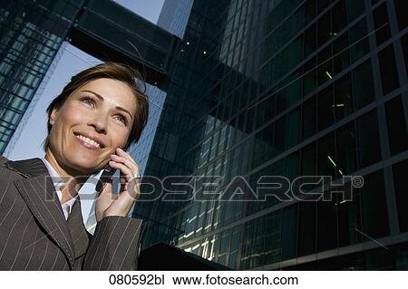 Stock Image - low angle portrait of mature businesswoman talking on mobile phone in front of office building. Fotosearch