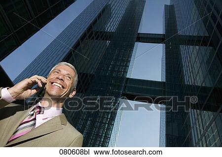 Stock Image - low angle portrait of mature businessman talking on mobile phone in front of office building. Fotosearch