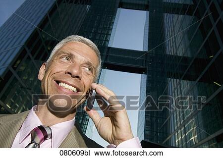 Stock Image - low angle portrait of mature businessman talking on mobile phone in front of office building. Fotosearch