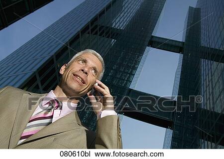 Stock Image - low angle portrait of mature businessman talking on mobile phone in front of office building. Fotosearch