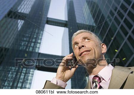 Stock Image - low angle portrait of mature businessman talking on mobile phone in front of office building. Fotosearch