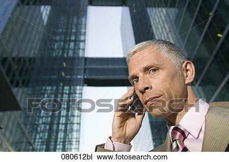 Stock Image - low angle portrait of mature businessman talking on mobile phone in front of office building. Fotosearch