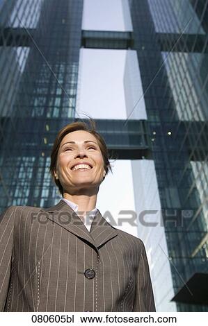 Stock Image - low angle portrait of smiling mature businesswoman in front of office building. Fotosearch