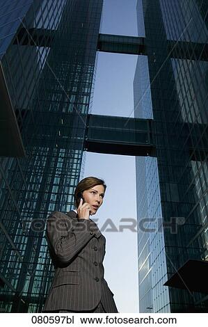 Stock Image - low angle view of mature businesswoman talking on mobile phone in front of office building. Fotosearch