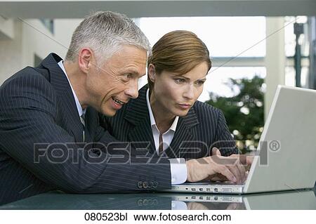 Stock Image - mature businessman and businesswoman working together with laptop computer. Fotosearch