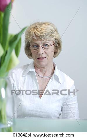 Stock Image - mature woman sitting at table with flowers. Fotosearch