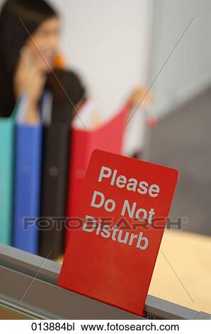Stock Image - Please do not disturb sign with woman having phone conversation in background. Fotosearch