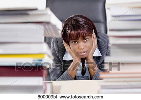 Stock Image - portrait of black businesswoman sitting behind piles of paper. Fotosearch