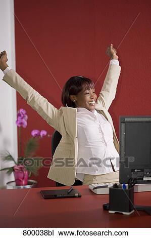Stock Image - portrait of black businesswoman sitting at desk stretching herself. Fotosearch