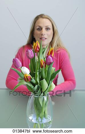 Stock Image - portrait of blonde woman with vase of tulips. Fotosearch