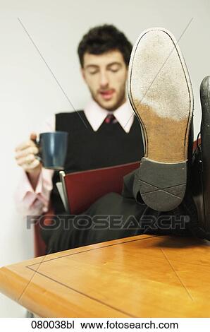 portrait of businessman sitting at table with his feet up holding mug and reading file View Large Photo Image Stock Image - portrait of businessman sitting at table with his feet up holding mug and reading file. Fotosearch