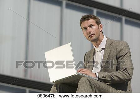 portrait of businessman sitting outdoors and working with laptop computer View Large Photo Image Stock Image - portrait of businessman sitting outdoors and working with laptop computer. Fotosearch