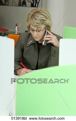 Stock Image - portrait of elderly female in office talking on cellphone and writing. Fotosearch