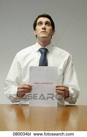 Stock Image - portrait of executive sitting at desk holding confidential document. Fotosearch