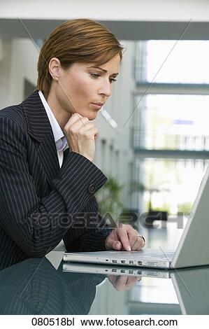 portrait of female executive sitting at table working with laptop computer View Large Photo Image Stock Image - portrait of female executive sitting at table working with laptop computer. Fotosearch