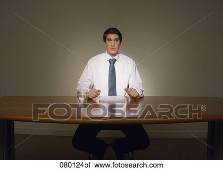 Stock Image - portrait of insecure businessman sitting at desk. Fotosearch