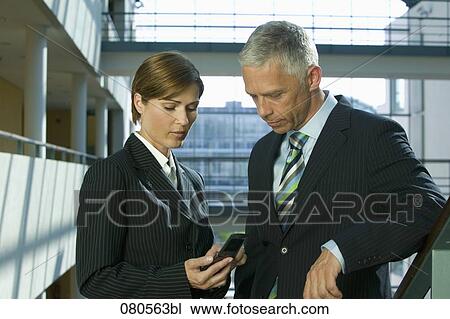 Stock Image - portrait of mature businesswoman and male colleague looking at mobile phone. Fotosearch