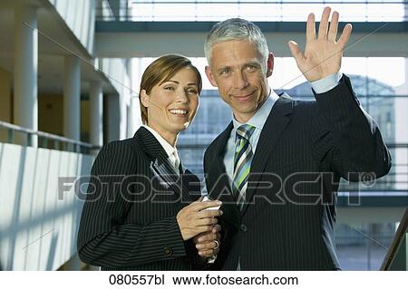 Stock Image - portrait of mature businesswoman with male colleague waving. Fotosearch