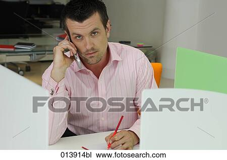 Stock Image - portrait of office worker sitting at desk talking on mobile. Fotosearch