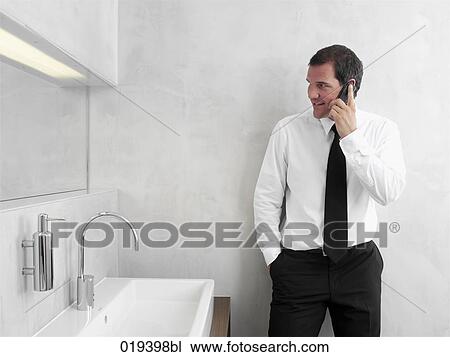 portrait of young businessman in front of mirror in bathroom talking on mobile phone View Large Photo Image Stock Image - portrait of young businessman in front of mirror in bathroom talking on mobile phone. Fotosearch