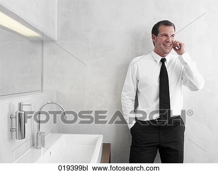 portrait of young businessman in front of mirror in bathroom talking on mobile phone View Large Photo Image Stock Image - portrait of young businessman in front of mirror in bathroom talking on mobile phone. Fotosearch