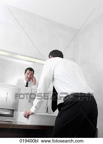portrait of young businessman in front of mirror in bathroom talking on mobile phone View Large Photo Image Stock Image - portrait of young businessman in front of mirror in bathroom talking on mobile phone. Fotosearch
